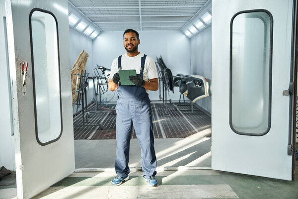 Young mechanic stands proudly in a bright workshop, ready to tackle his tasks for the day.