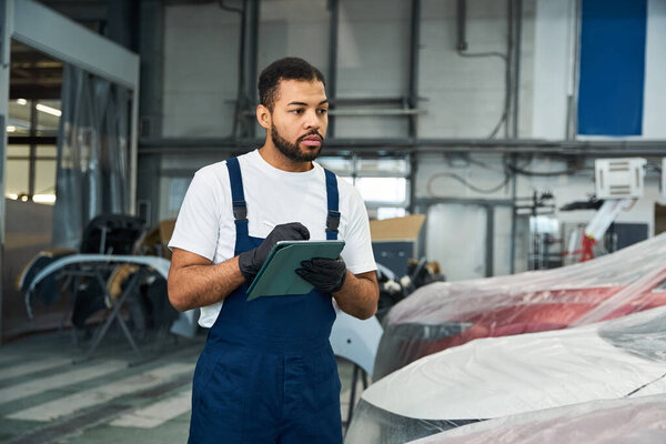 Опытный механик внимательно изучает детали автомобиля, делая заметки на работе..