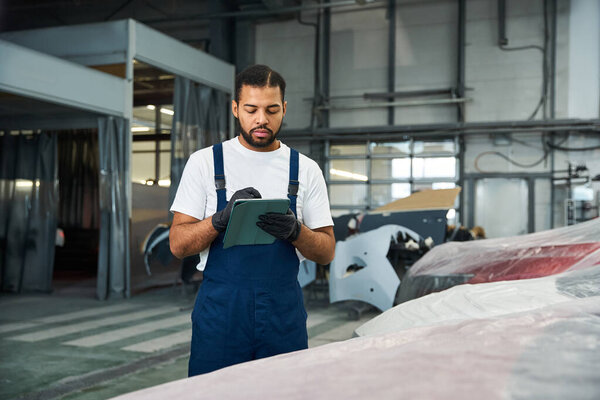Опытный молодой человек изучает детали автомобиля и делает заметки в хорошо оборудованной автомастерской