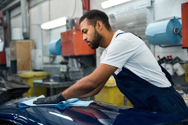 Молодой механик тщательно чистит транспортное средство в яркой, занятой автомастерской.