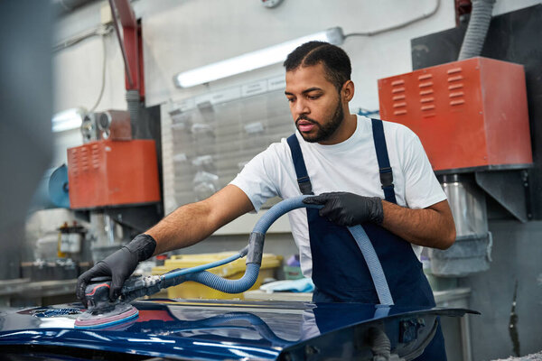 Handsome young mechanic working diligently on a cars surface in a vibrant auto shop