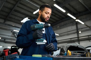 Yetenekli genç bir tamirci meşgul bir oto tamirhanesinde elektrikli bir alet kullanmaya odaklanır..