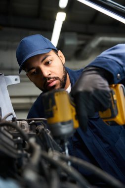 Yakışıklı tamirci garajda elektrikli aletler kullanırken makineleri tamir etmeye dikkatle odaklanır.