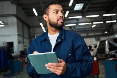 Yakışıklı genç tamirci, modern bir otomotiv tamirhanesinde çalışma programını inceliyor..