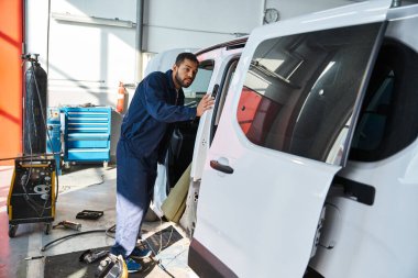 Güneş ışığı atölye pencerelerinden geçerken genç tamirci minibüsü teftiş ediyor