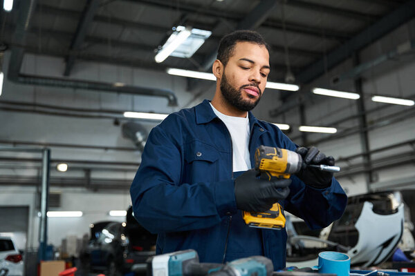 Handsome young mechanic focuses intently on a power tool in a busy garage setting.