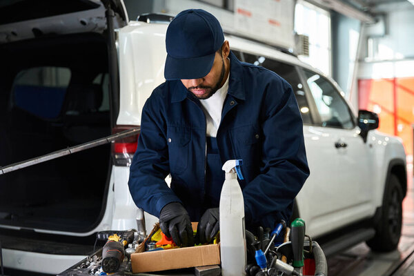 Красивый молодой человек фокусируется на организации инструментов во время ремонта автомобиля в гараже.