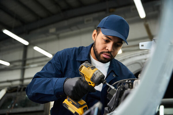 Handsome mechanic focuses intently on repairing an engine with his power tool in the workshop.