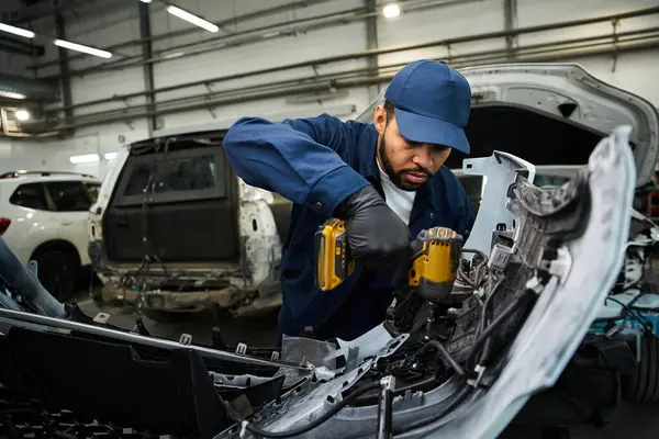 Genç tamirci yoğun bir oto tamirhanesinde araba parçalarını tamir ederken dikkatle odaklanıyor.