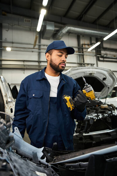 Focused young mechanic holds power tools while inspecting a car in a well lit workshop environment