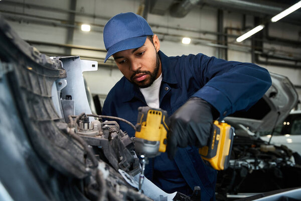 A skilled mechanic uses power tools diligently on a vehicle in a bright workshop.