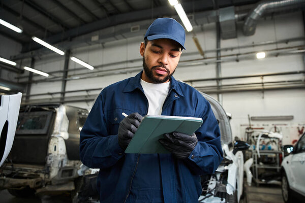 Молодой механик сосредоточился на своей работе, делая заметки, стоя в оживленном автомобильном магазине.