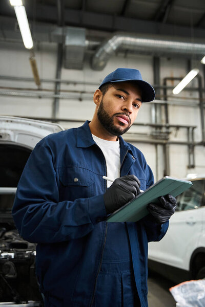 Красавчик-механик оценивает состояние автомобиля, записывая заметки в оживленном гараже.