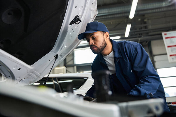 Handsome mechanic works diligently under the hood of a vehicle, ensuring everything is in order.