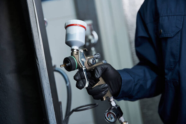 Опытный молодой механик, работая в ярком гараже, применяет краску с помощью аэрозоля.