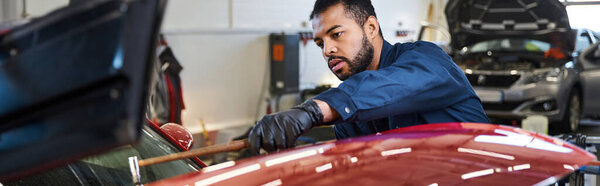 Молодой человек тщательно работает над автомобилем при ярком свете в оживленном гараже.