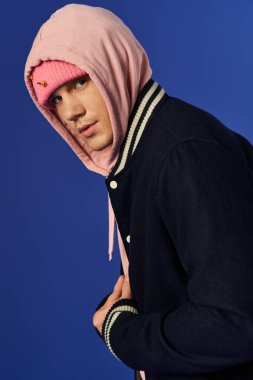 Pembe kapüşonlu şık genç adam mavi arka planda rahatça poz veriyor..