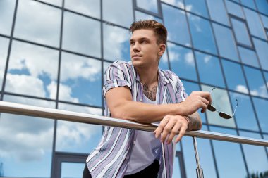 Young man leans thoughtfully against a railing, enjoying the view. clipart