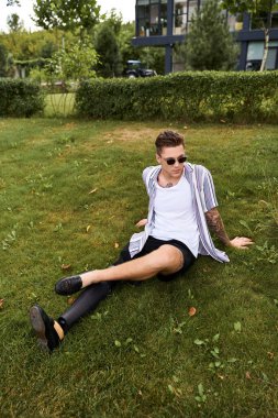 Protez bacaklı genç adam açık yeşil çimenlerde otururken güneşli bir günün tadını çıkarıyor..