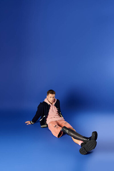 A young man with a prosthetic leg sits relaxed on the floor showcasing a stylish outfit.