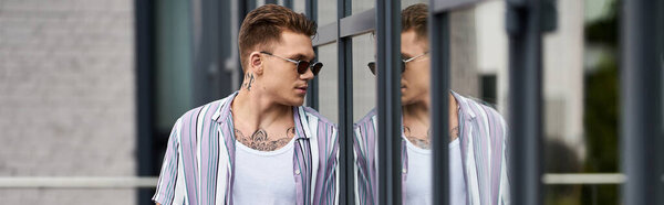 Young man strolls confidently alongside modern reflective buildings.