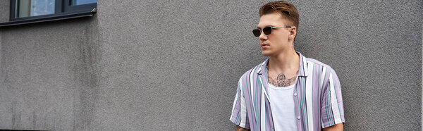 Красивый молодой человек демонстрирует стиль и уверенность рядом с серой стеной.