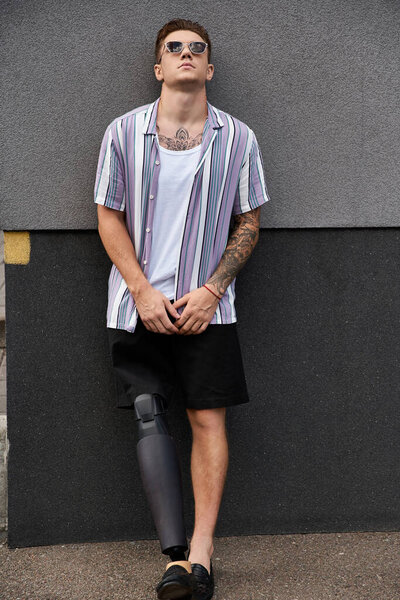 Young man with a prosthetic leg stands against a wall, showcasing his style and confidence.
