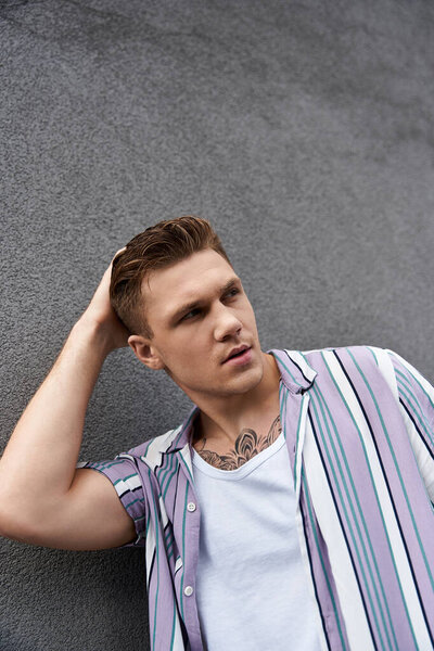 Молодой человек уверенно позирует, выражая стильное поведение и уникальность.