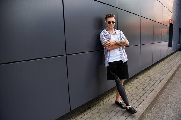 Молодой человек с протезной ногой уверенно позирует возле гладкого городского здания.