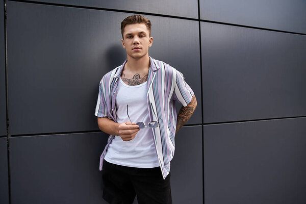 Молодой человек стильно стоит у стены современного здания.