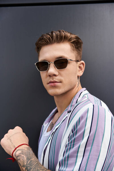 Молодой человек с татуировками демонстрирует свой стиль и уверенность, позируя небрежно.