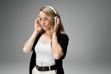 A young woman with vitiligo enjoys music with headphones in a minimalist setting. clipart