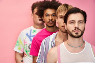 Four men in vibrant clothing pose against a pink background, showcasing pride and unity. clipart