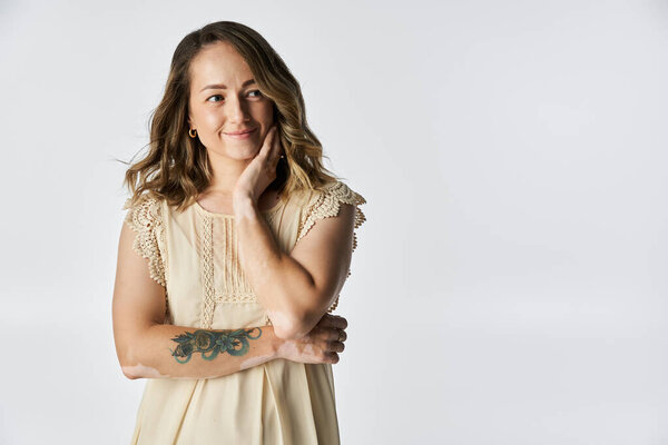 Молодая женщина с витилиго мягко улыбается, положив руку на щеку, демонстрируя свою красоту.