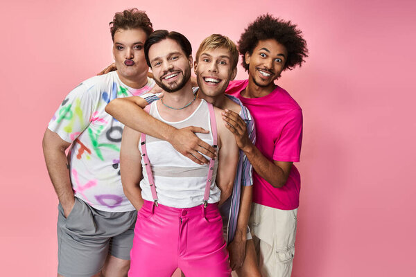 Friends in vibrant outfits embrace joy and pride against a pink background.