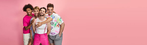 Four friends pose joyfully against a pink backdrop, showcasing their vibrant pride themed outfits.