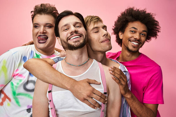 Four individuals embrace joyfully, showcasing colorful fashion and pride in a vibrant setting.