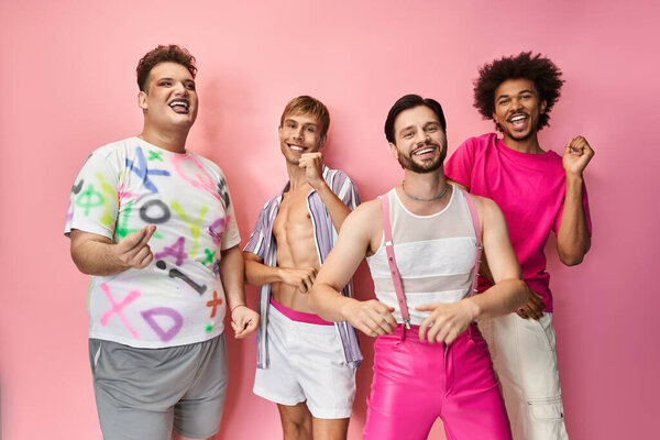 Four friends show pride and joy in colorful outfits against a pink backdrop.