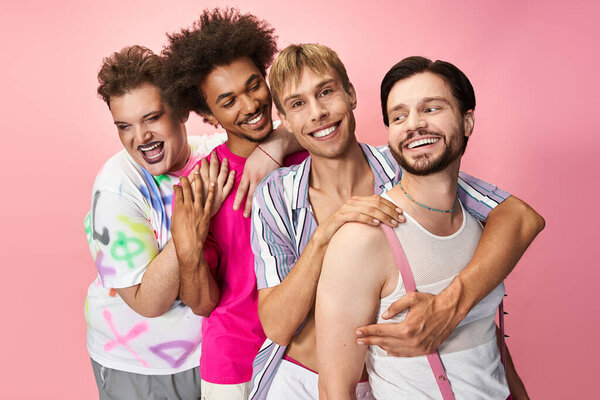 Four individuals express joy and pride in their vibrant, colorful outfits against a pink backdrop.