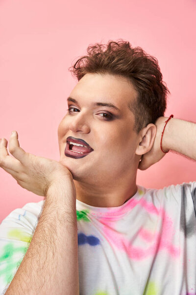 Individual showcases bold queer style with vibrant makeup and joyful attitude in bright setting.