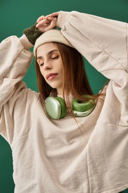 Uzun saçlı, örgü şapkalı ve büyük kazaklı genç bir kadın özenle müzik dinliyor..