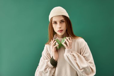 Kulaklıklı genç bir kadın yeşil bir arkaplanda poz veriyor, güzelliğini ve gücünü gösteriyor..