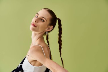 Genç bir kadın yeşil bir geçmişe karşı özgüvenle poz veriyor, mücadelesinde direnç gösteriyor..