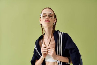 Saçları örgülü, kendine güvenen genç bir kadın canlı yeşil bir zemine karşı duruyor..