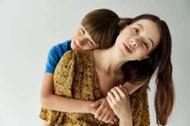 Genç bir anne oğlunu sevgiyle kucaklıyor. Her ikisi de parlak bir stüdyo ortamında günlük giysiler içinde..