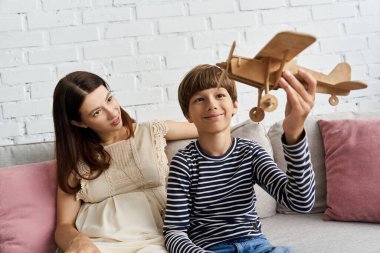 Bir anne ve oğlu, rahat oturma odalarında tahta bir oyuncak uçakla neşe içinde oynuyorlar..