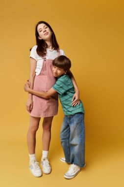 Genç bir anne, bir stüdyoda kendisine şakayla sarılan oğluyla güvenle ayakta duruyor..