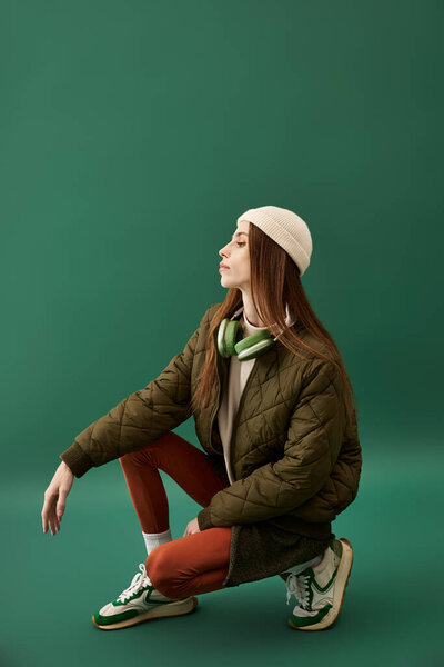 Young woman with anorexia sits thoughtfully against a green backdrop in casual attire.
