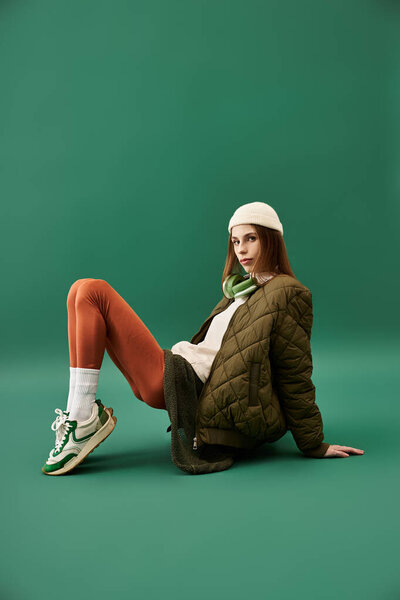 A young woman in casual attire rests against a green backdrop, reflecting her battle with anorexia.