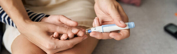 Молодая мать помогает сыну проверить уровень сахара в крови дома, баннер